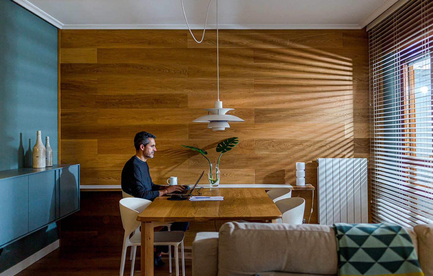 Mann sitzt im Homeoffice am Holztisch vor einer Holzwand